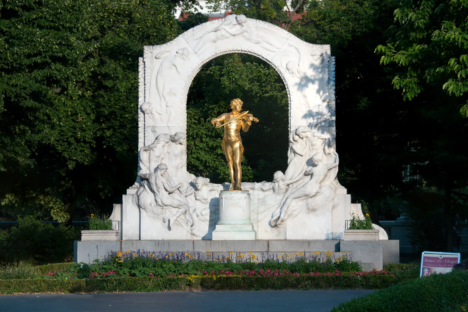 Das vergoldete Standbild von Johann Strauss II. mit der Violine, vor einem Marmorbogen im Stadtpark in Wien